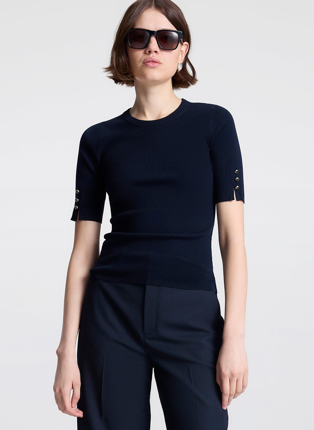 Person wearing a navy blue outfit with decorative buttons on a light gray background