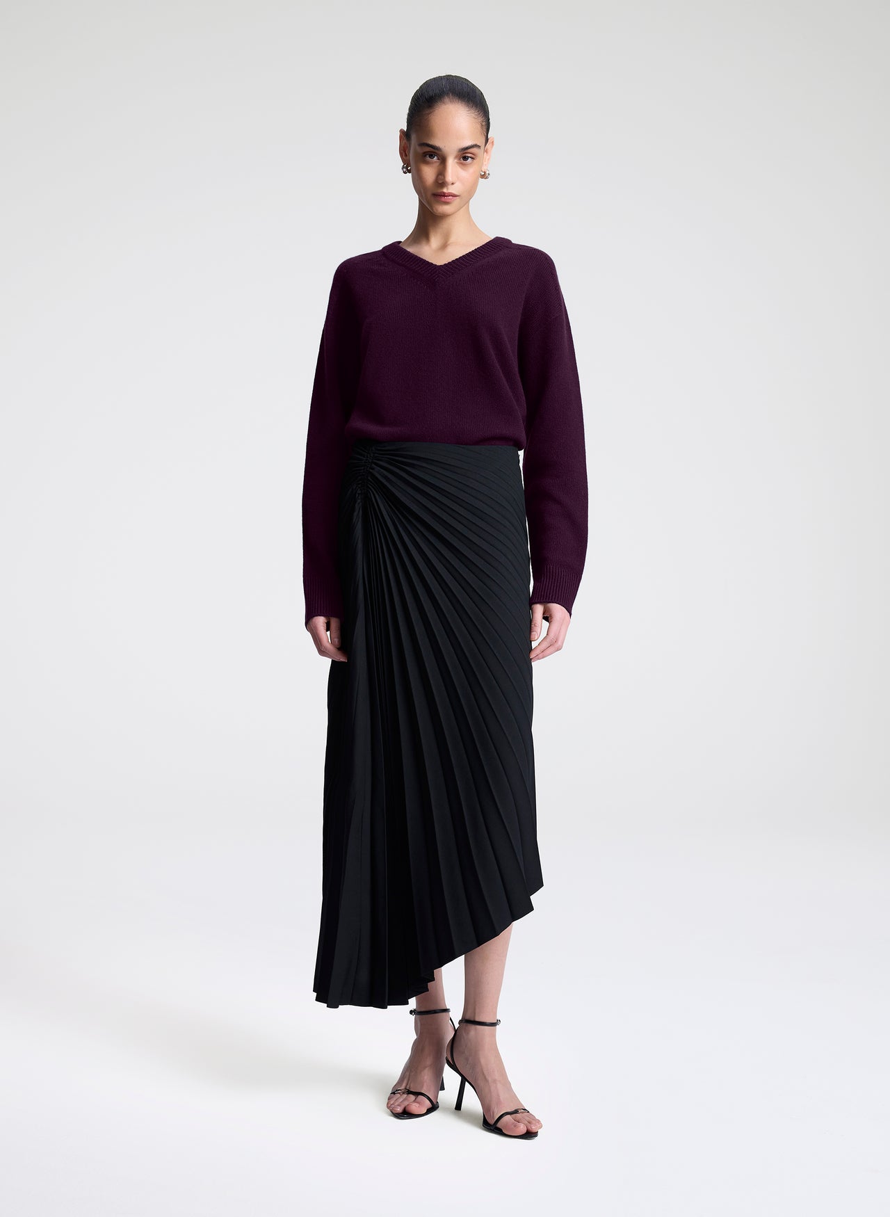 Woman wearing a dark purple sweater and black skirt on a white background