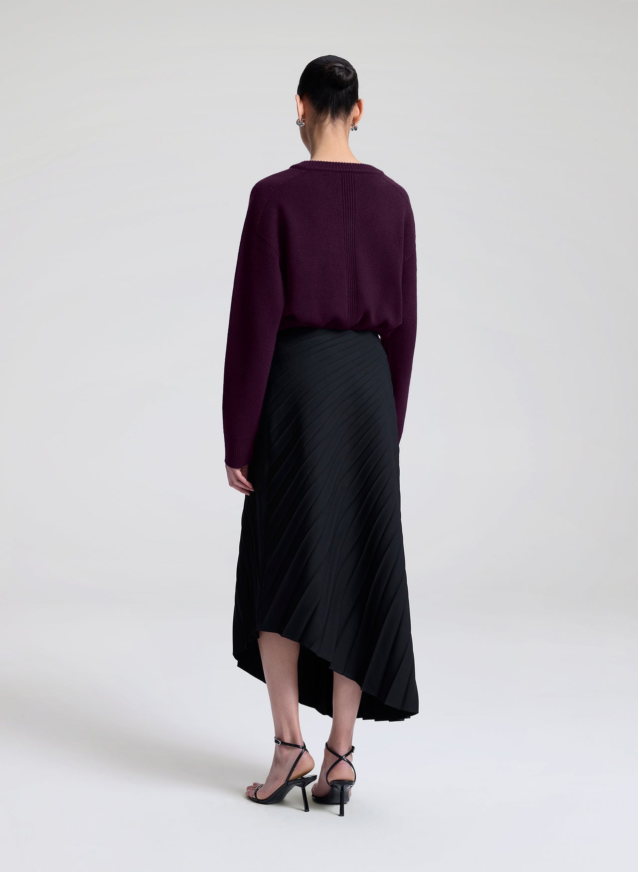 Woman wearing a dark purple top and black skirt on a white background